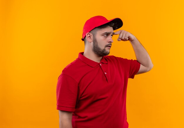 빨간 유니폼과 모자에 젊은 배달 남자는 그의 사원을 가리키는 혼란 찾고