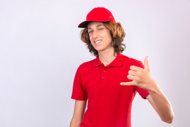 Young delivery man in red uniform making call me gesture looking confident over isolated white background