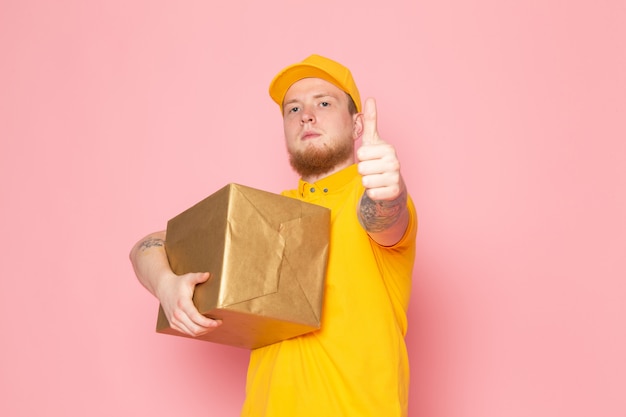young delivery man in yellow polo yellow cap white jeans holding a box on pink