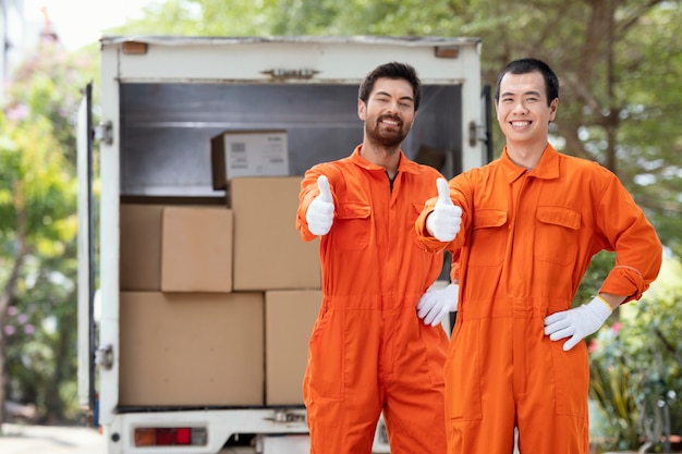 Free photo young delivery men showing ok sign near delivery car