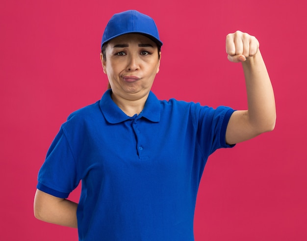 青い制服とキャップの若い出産の女性は、拳を上げるのに混乱しました