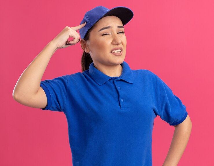 無料Photo ピンクの壁の上に立っている彼女の頭を引っかいて混乱しているように見える青い制服と帽子の若い出産女性