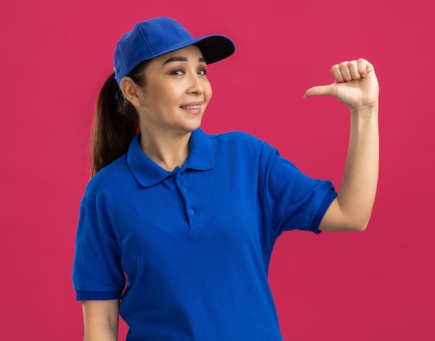 Foto gratuita giovane donna delle consegne in uniforme blu e berretto sorridente fiducioso