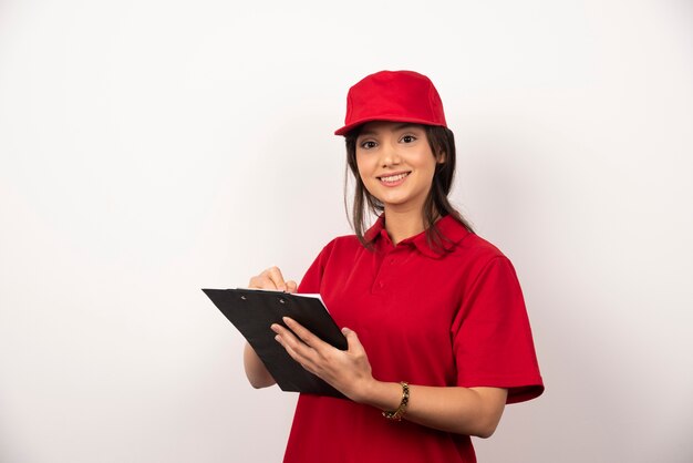 Young delivery woman in red uniform with clipboard on white background.