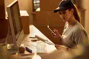 Free photo young delivery woman using mobile phone while going through dispatch list in the office