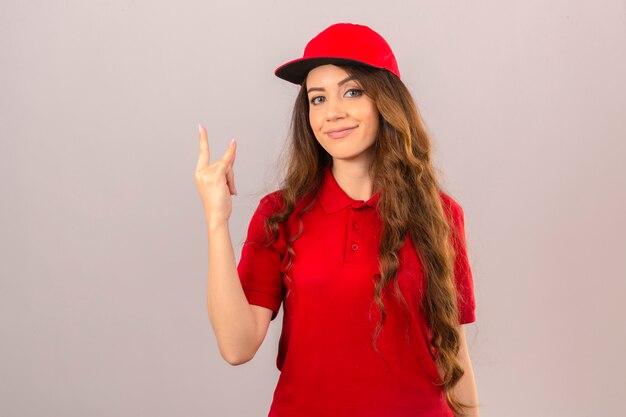 빨간 폴로 셔츠와 모자를 입고 젊은 배달 여자 빨간 폴로 셔츠와 모자를 입고 젊은 배달 여자는 격리 된 흰색 배경 위에 친절 미소 피자 상자와 함께 서