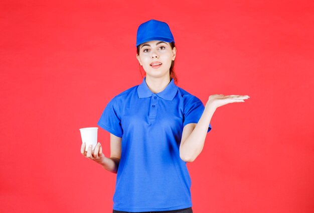 赤にお茶のプラスチックカップを保持している青い帽子の若い配達員。