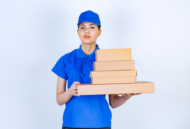 Young deliverywoman in blue uniform holding cardboard boxes on white background.