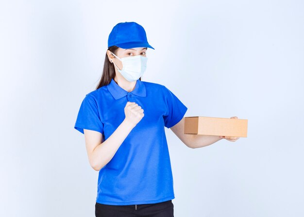 Young deliverywoman in medical mask holding carton box on white background. 