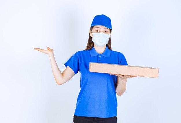 Young deliverywoman in medical mask holding carton package. 