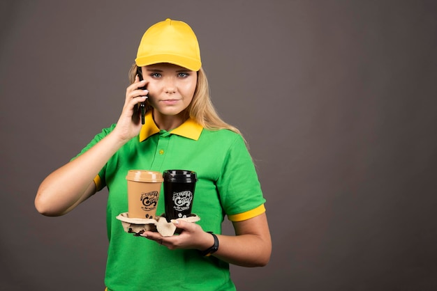 Giovane donna delle consegne con tazze di caffè parlando sullo smartphone. foto di alta qualità