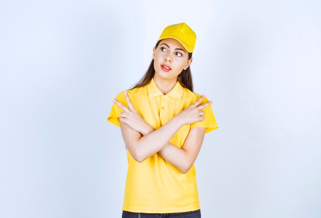 Young deliverywoman in yellow t-shirt and cap pointing at somewhere on white.