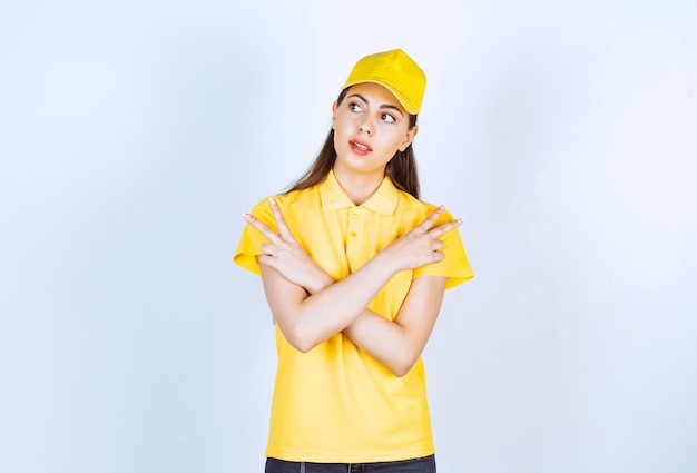 Молодая доставщица в желтой футболке и кепке, указывая куда-то на белом.