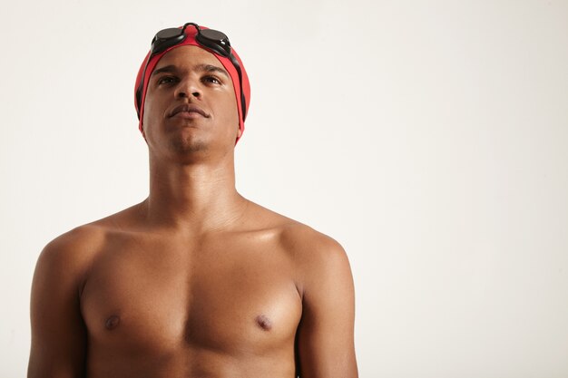 young determined-looking African American swimmer wearing red cap and black goggles looking up on white