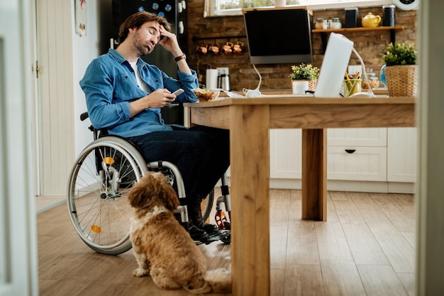 Young disabled entrepreneur having a headache while using mobile phone on lunch break at home.