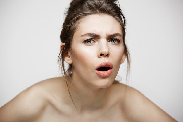 Young displeased brunette girl with funny face looking at camera with opened mouth over white background.