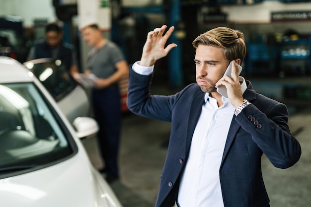 車の修理ワークショップにいる間電話で話している若い不機嫌なビジネスマン