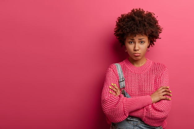 Young displeased ethnic woman crosses arms over body, looks sadly