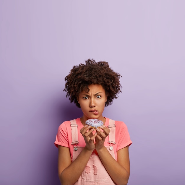 Free photo young displeased woman holds delicious sweet doughnut