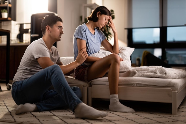 Young displeased woman ignoring her boyfriend who is trying to apologize after a quarrel in the bedroom