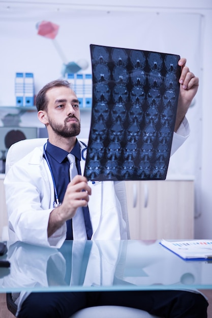 Foto gratuita giovane medico al gabinetto della clinica che tiene una radiografia del cervello. medico che controlla la scansione cerebrale di un paziente.