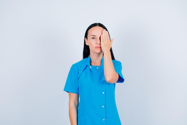 Young doctor is covering her right side of face with hand on white background