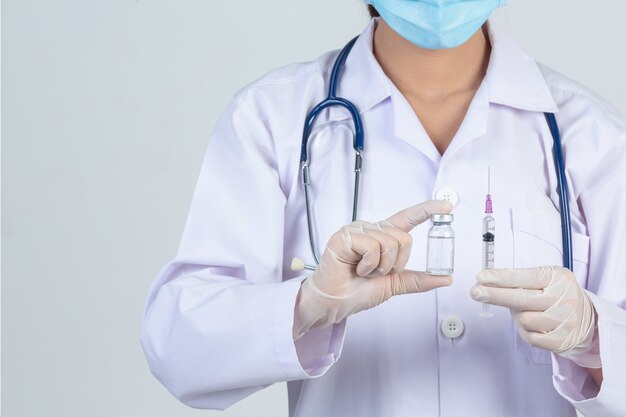 젊은 의사는 회색 벽에 백신 유리 병 고무 장갑과 피하 주사기를 들고있다.