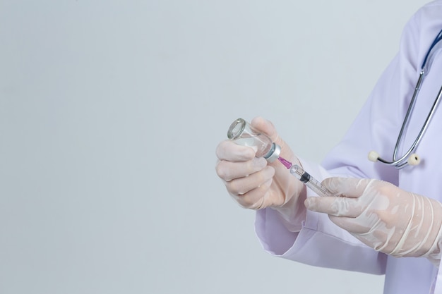 若い医者は灰色の壁にワクチンバイアルゴム手袋で皮下注射器を保持しています。