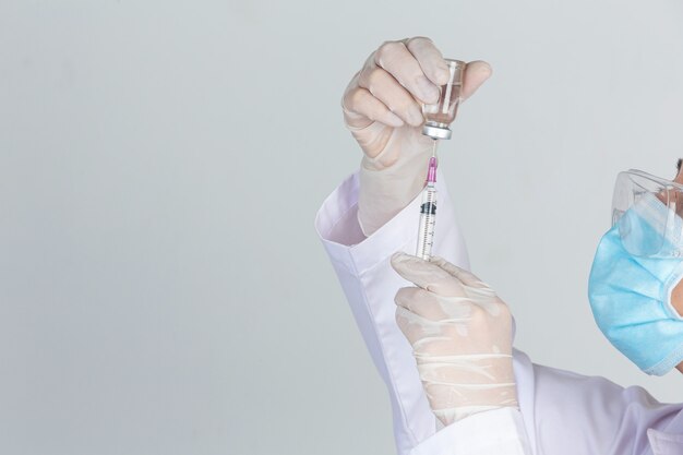 Young doctor is  holding  hypodermic syringe with  vaccine vial  rubber gloves on gray wall.