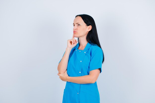 Young doctor is thinking by holding forefinger on cheek on white background