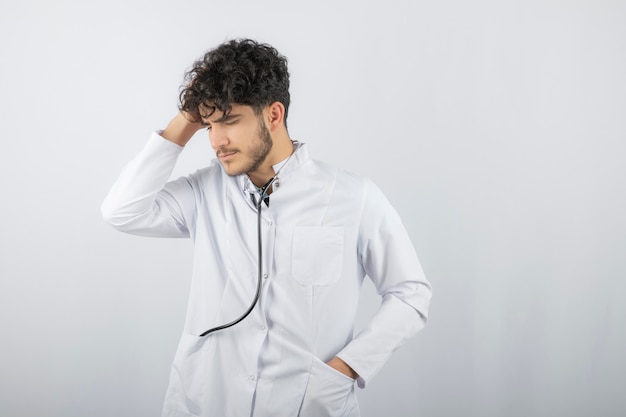 Young doctor is upset and holding his hand to his head, looking down.