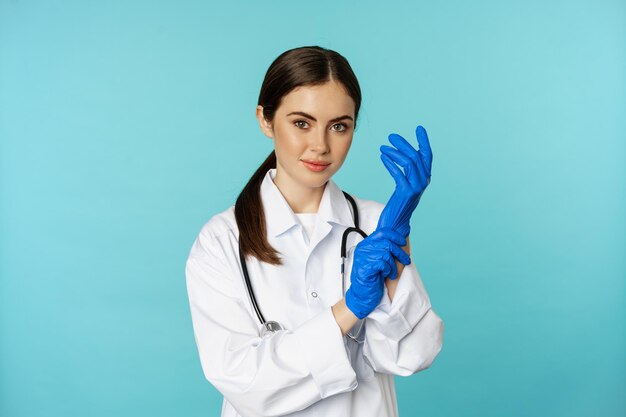 Young doctor professional physician woman put on gloves smiling at camera ready for medical checkup ...