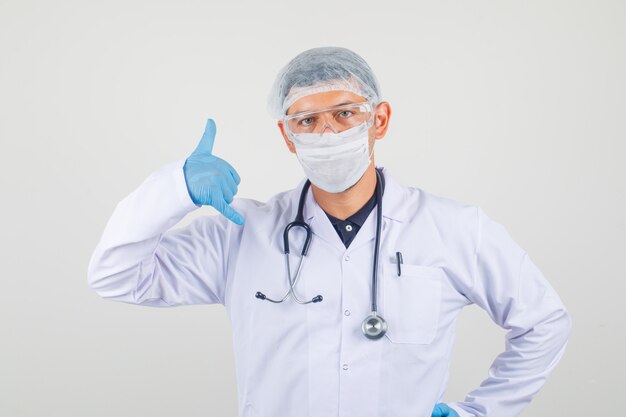 Young doctor showing call me gesture in white coat, hat and gloves