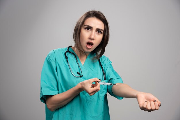 Young doctor in uniform injecting herself with syringe. High quality photo