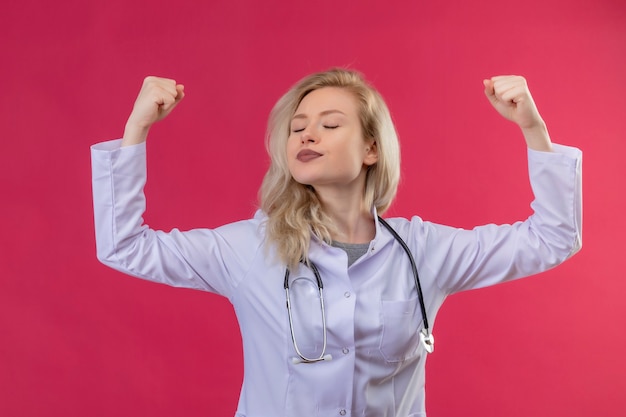 young doctor wearing stethoscope in medical gown doing stong gesture on red backgroung