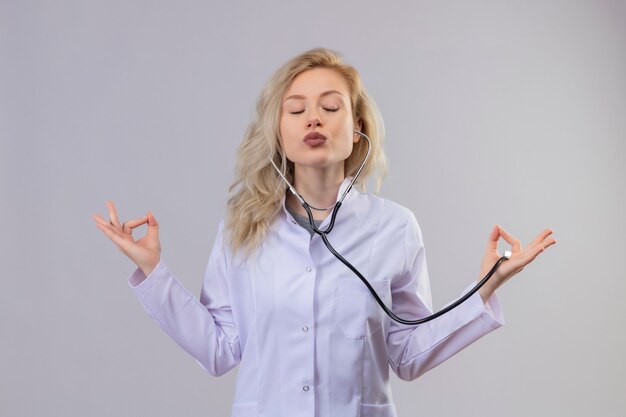 Free photo young doctor wearing stethoscope in medical gown showing okey gesture on white wall