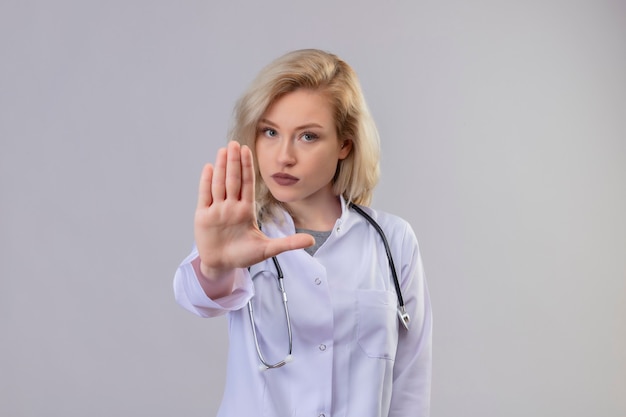 Молодой врач со стетоскопом в медицинском халате показывает жест стоп на белой стене