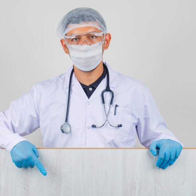 Young doctor in white coat, hat, gloves showing wooden board