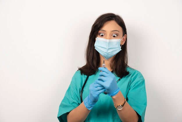 Young doctor with medical mask preparing injection on white background.