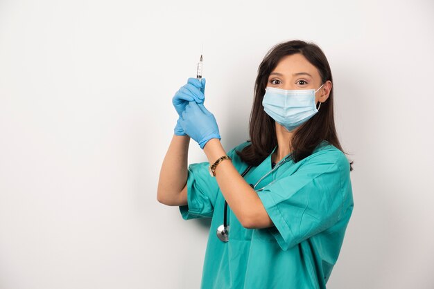 Young doctor with medical mask and syringe on white background.