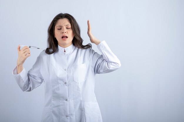young doctor with syringe screaming on white wall. 
