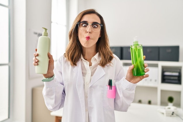 Free photo young doctor woman holding aloe vera and cream making fish face with mouth and squinting eyes crazy and comical
