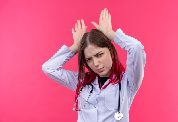  young doctor woman wearing stethoscope medical gown showing bunny ears gesture on pink isolated wall