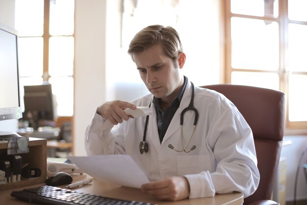 Young doctor working in his office with windows on the background