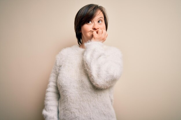 Young down syndrome woman standing over isolated background looking stressed and nervous with hands on mouth biting nails Anxiety problem