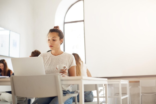 Young educator using laptop computer to run an online class on graphic design working in a crowded studio space Education concept