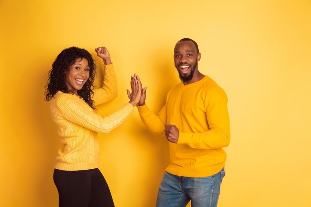 노란색 배경에 포즈 밝은 캐주얼 옷에 젊은 감정적 인 아프리카 계 미국인 남자와 여자. 아름다운 커플. 인간의 감정, 얼굴 expession, 관계, 광고의 개념. 팀워크.