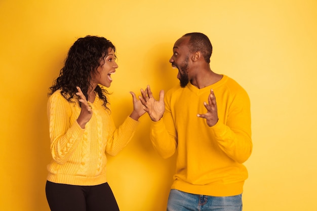 Молодой эмоциональный афро-американский мужчина и женщина в яркой повседневной одежде позирует на желтом пространстве