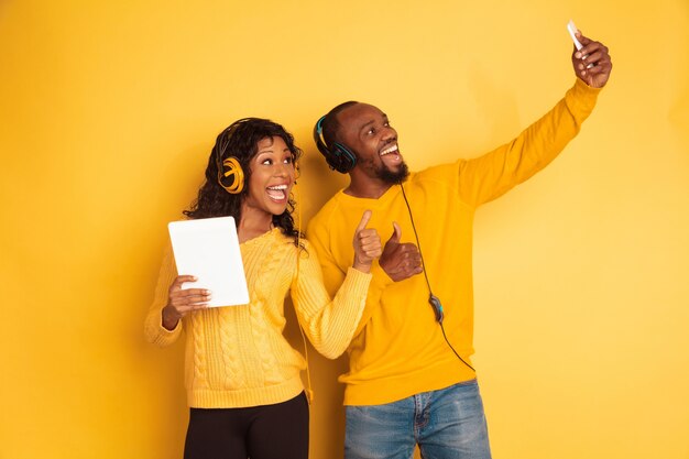 Young emotional african-american man and woman in bright casual clothes on yellow space. Beautiful couple