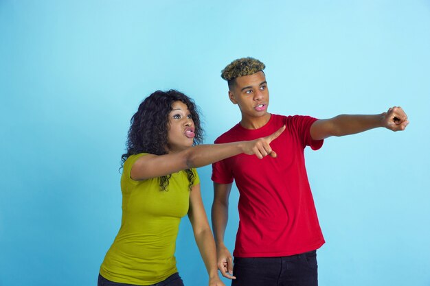 Young emotional african-american man and woman Totally shocked look at side like sport fans on blue